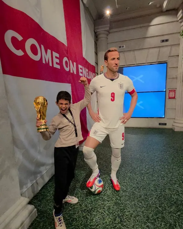 طالب يحمل مجسّمًا لكأس العالم بجانب تمثال شمعي للاعب كرة قدم