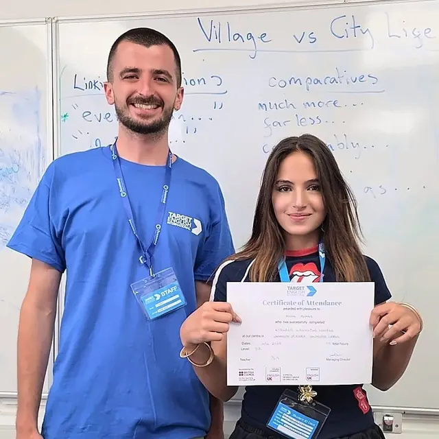 فتاة تحمل شهادة الحضور إلى جانب أحد أفراد طاقم المدرسة